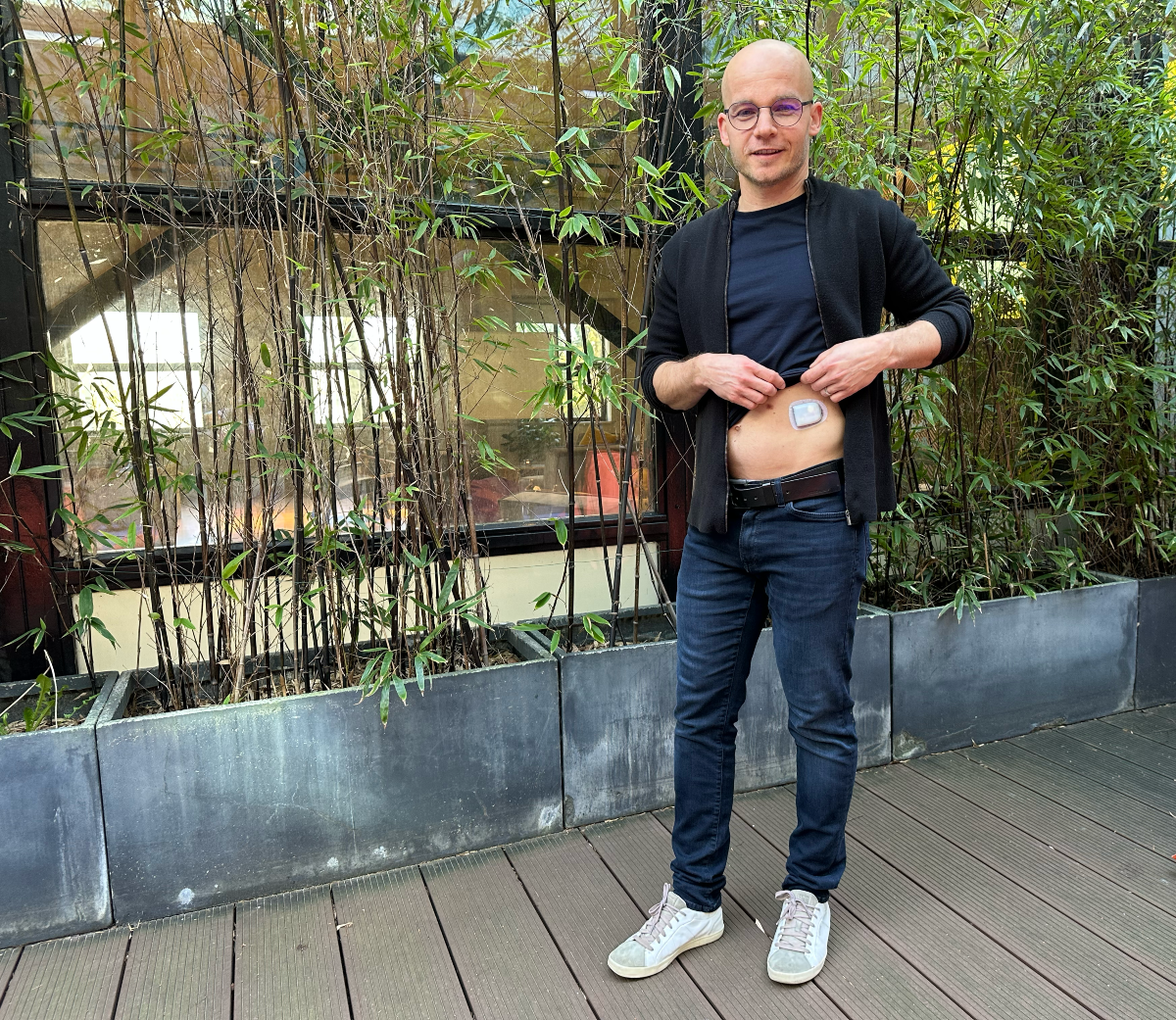Omnipod Podder Tom Vesely standing in front of plants with his shirt raised to show a Pod on his stomach