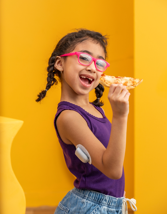 Omnipod Podder, Amy, standing against an orange backdrop while holding a slice of pizza