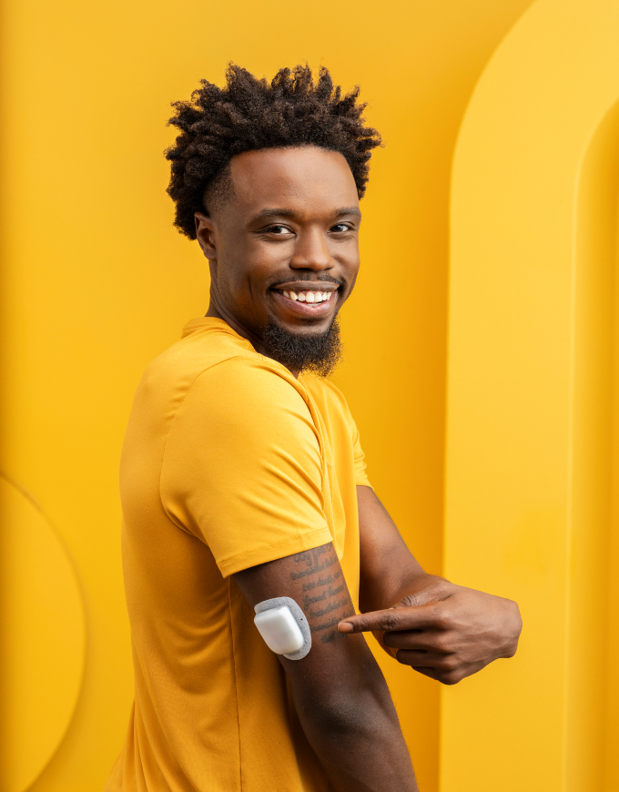 Omnipod Podder, Enoch, standing against an orange backdrop pointing to his Pod on his right arm