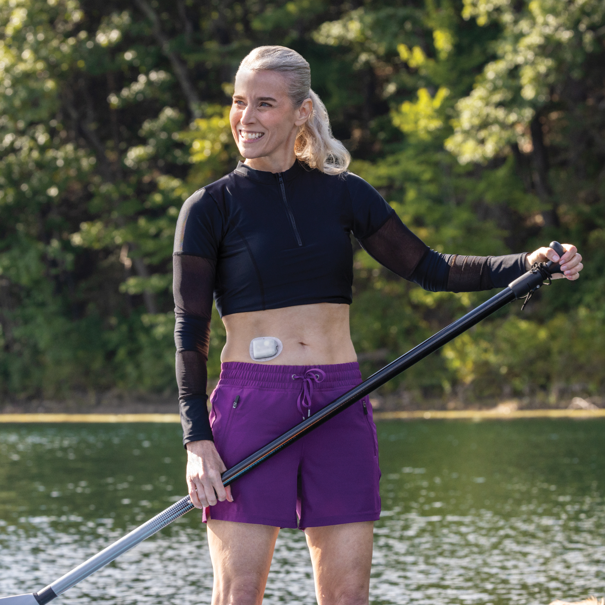 Omnipod Podder, with a Pod on their stomach, on a paddle board on the waters