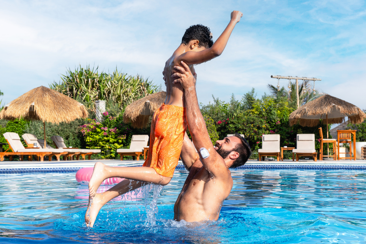Man, with a Pod on his left arm, in pool holding up son