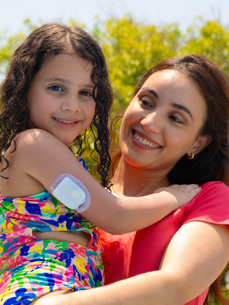 smiling mom holding daughter with a pod on back of her arm