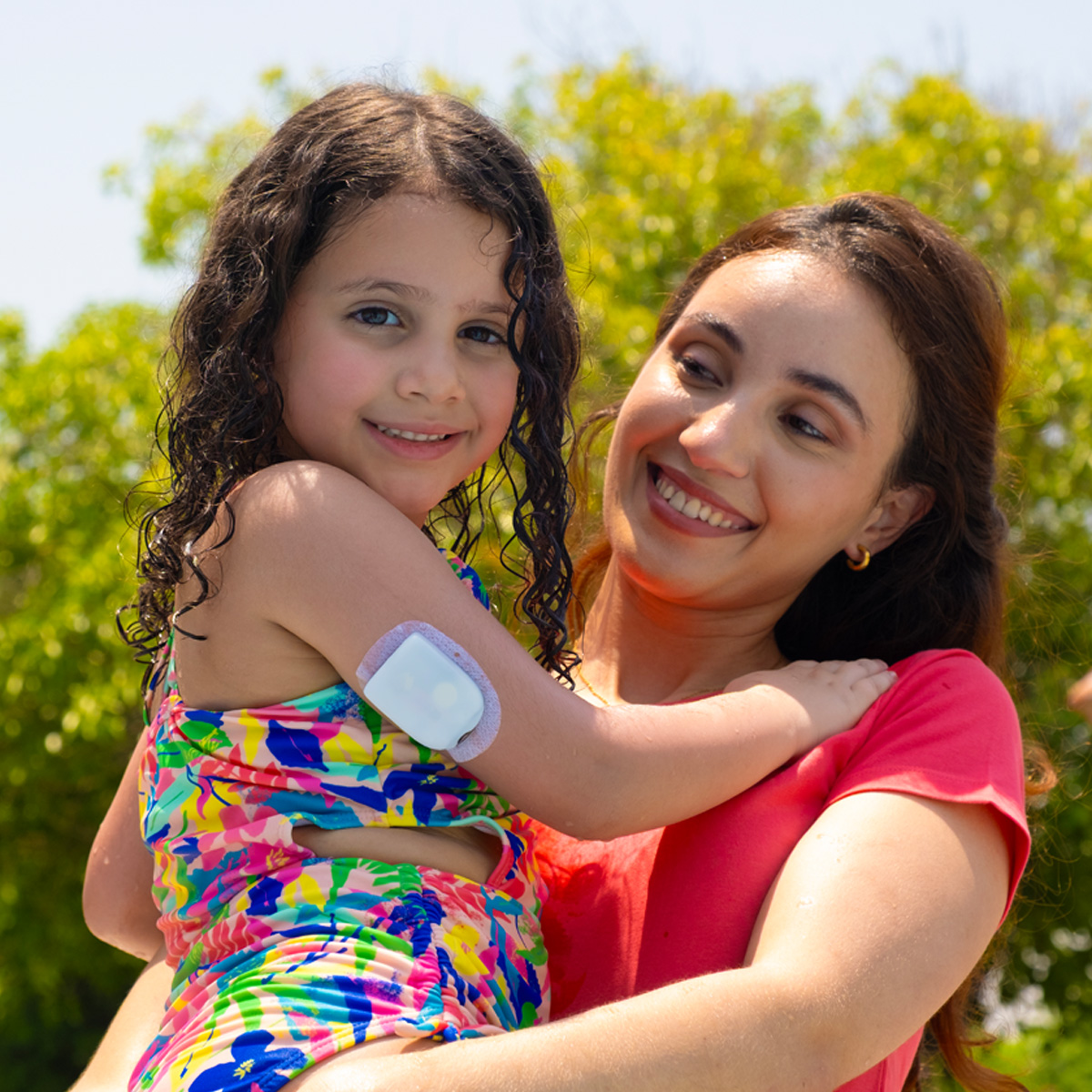 mom holding and smiling at daughter who is wearing a pod on her arm
