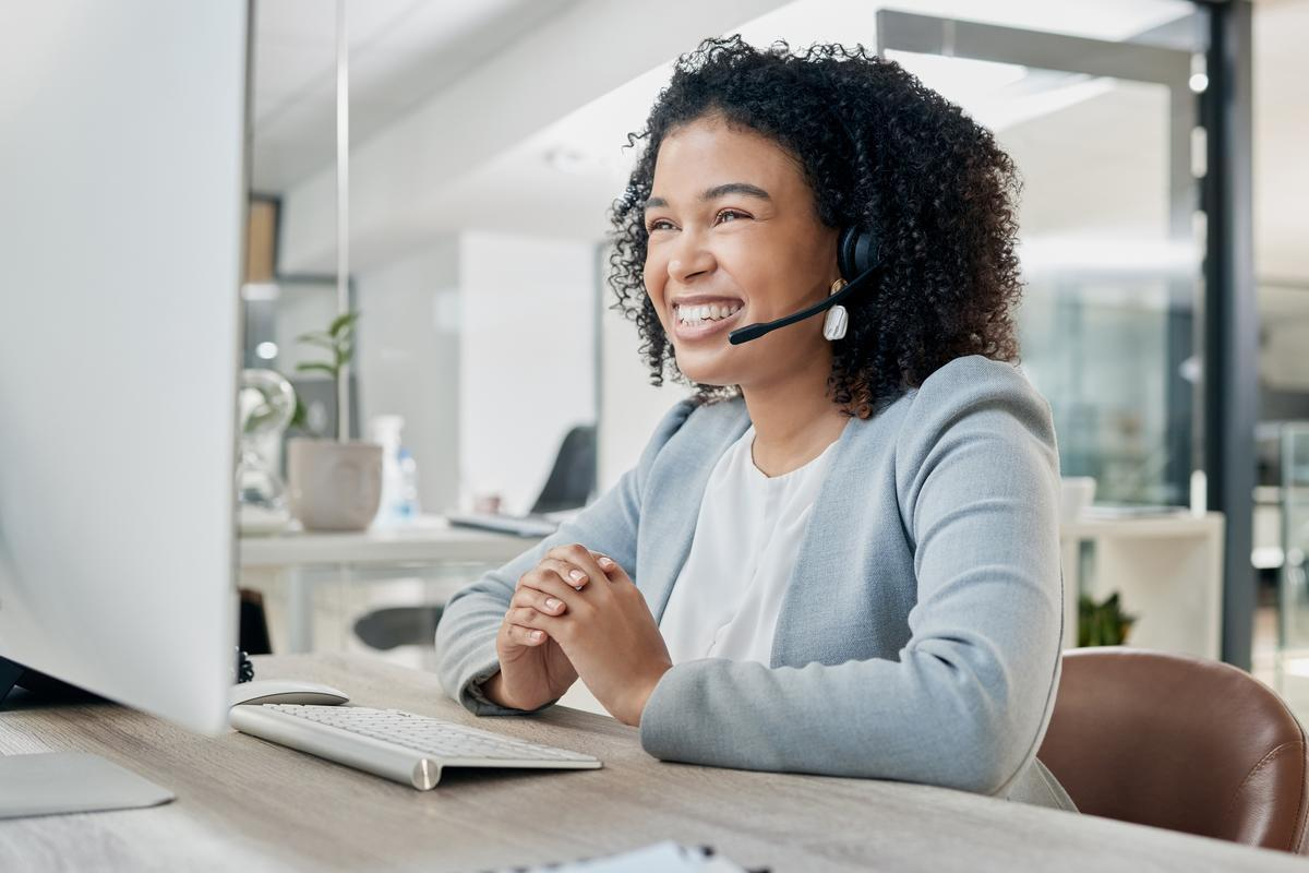 Girl in front of a computer smiling with a headset on and wearing a blue jacket