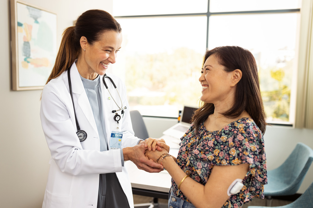 Female HCP holding hands with female patient with a Pod on her arm