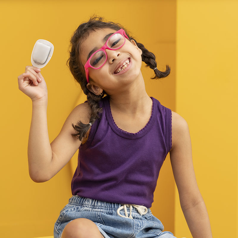 Young podder, sitting down against an orange background, holding an Omnipod up high