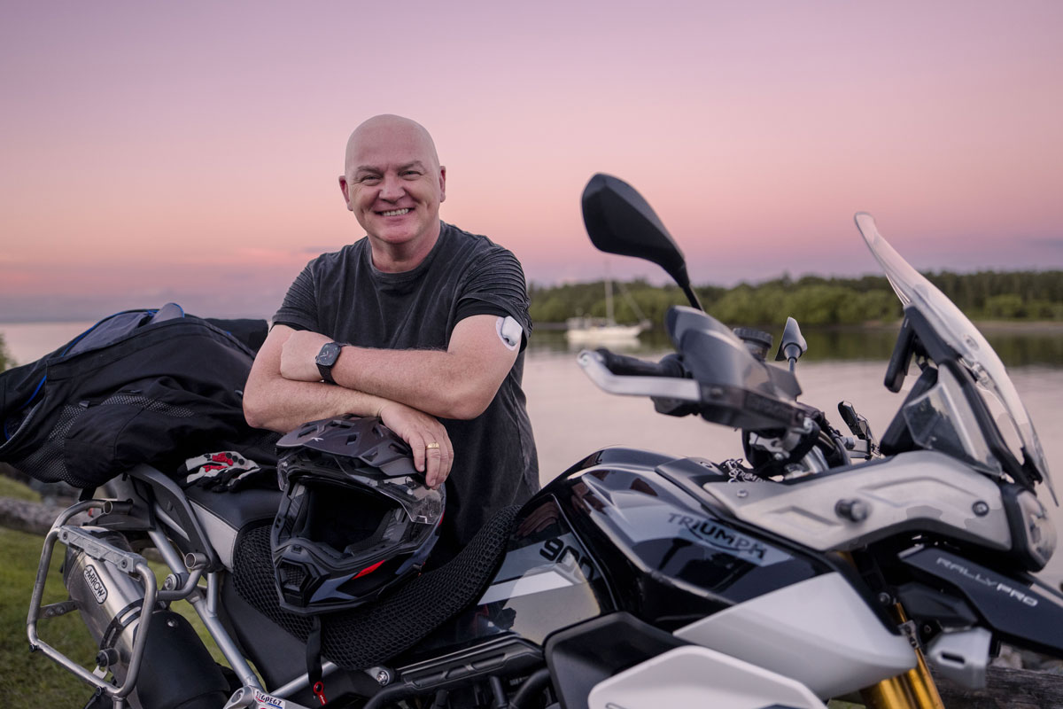 Man sitting on motorcycle smiling while wearing a pod on his arm