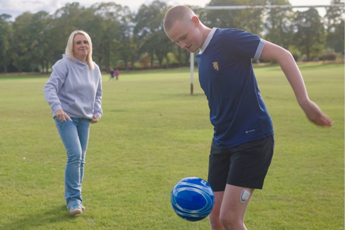 Podder, playing football outside on the grass, wearing an Omnipod