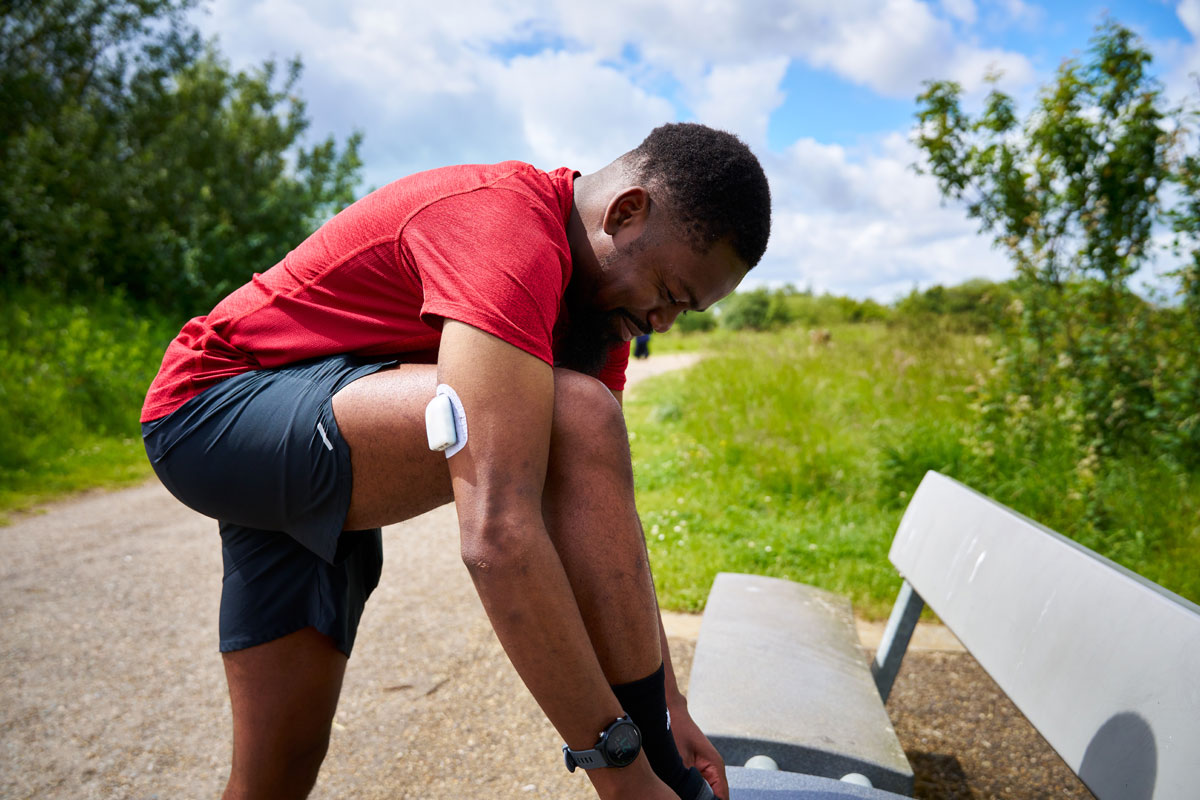man wearing a pod on his arm is bent tying his shoe on a bench