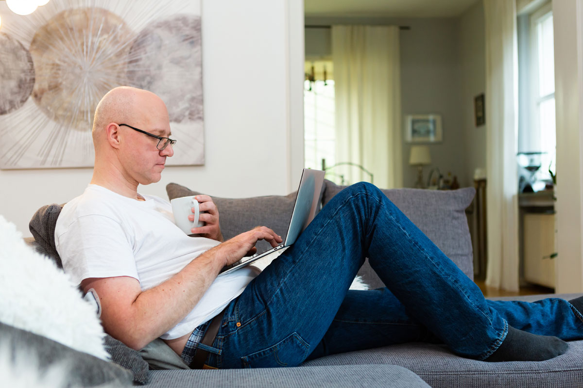 man sitting on couch with laptop propped on legs