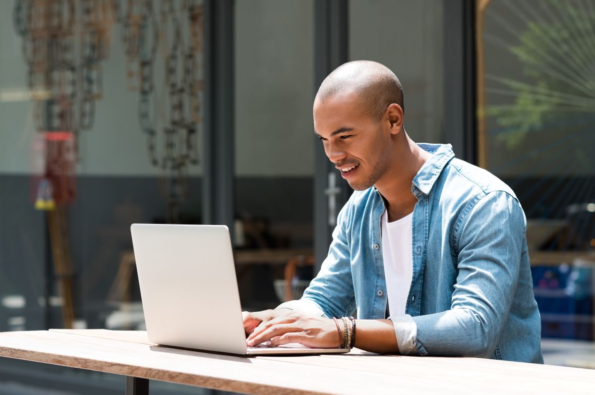 Male sitting outside with his laptop on a table