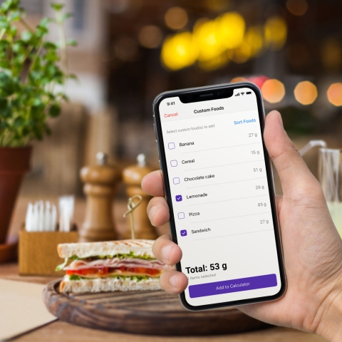 hand holding phone with custom food selections and sandwhich in background