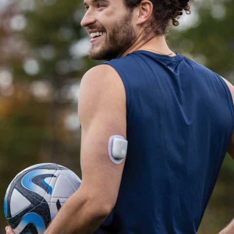 Man outside holding a football wearing an Omnipod 5