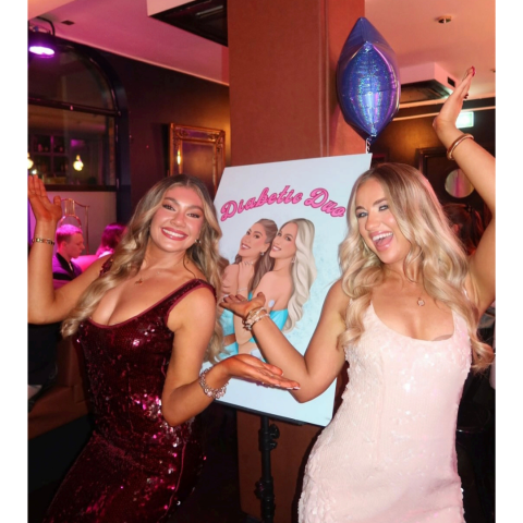 Omnipod Podder, Beth McDaniel, at a nightclub with her friend and a sign that says, "Diabetic Duo" in the background